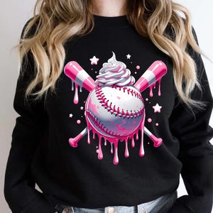 May include: Black sweatshirt with a baseball-themed design. The baseball has pink dripping details, crossed pink and white striped bats, and a swirl of whipped cream. White stars are scattered around the design, creating a playful aesthetic.