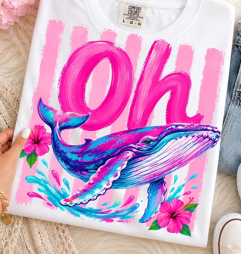 Pu&ograve; includere: Una t-shirt bianca con una grande scritta rosa a pennellata che recita Oh, accompagnata da una balena blu e viola. Il design presenta strisce verticali rosa, fiori di ibisco rosa acceso e spruzzi d'acqua blu sulla parte anteriore.