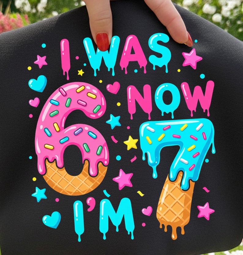 May include: Black graphic design with the text "I WAS 6 NOW I'M 7". The numbers 6 and 7 are designed as donuts and ice cream cones. Pink, blue, yellow, and orange colors are used in the design.