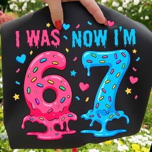 May include: Black fabric with the text "I WAS NOW I'M" in pink and blue. The numbers "67" are designed to look like melting donuts, with sprinkles and heart and star accents. A fun, colorful design for a birthday celebration.