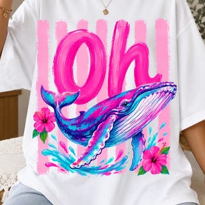 Pu&ograve; includere: Una t-shirt bianca con la scritta Oh in grandi lettere rosa effetto pennellata, una balena blu e rosa che nuota tra spruzzi d'acqua e due fiori di ibisco rosa acceso su uno sfondo a righe verticali rosa.