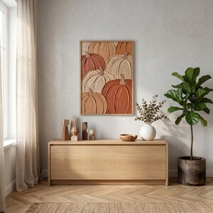 May include: A rectangular wall art piece featuring a textured, impasto-style painting of multiple pumpkins in shades of orange, terracotta, and cream, enclosed in a light-toned wooden frame and displayed above a long, light-colored wooden console table.