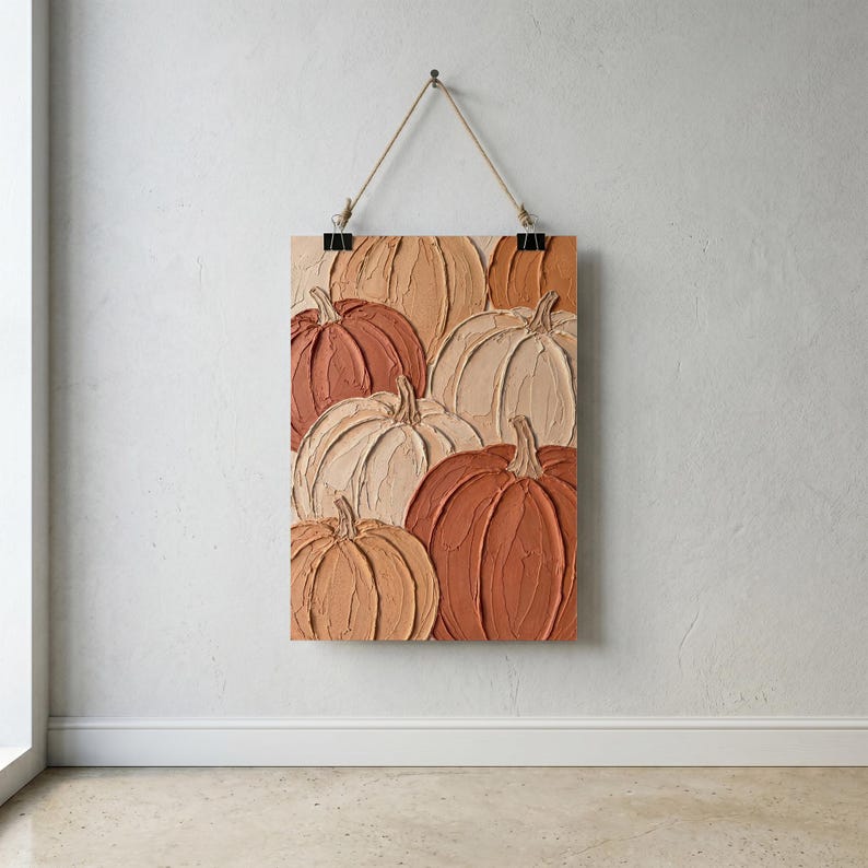 May include: A rectangular wall hanging featuring a textured impasto painting of multiple pumpkins in shades of cream, beige, tan, and burnt orange. The artwork is suspended by a thin rope attached to two black metal clips at the top edge.