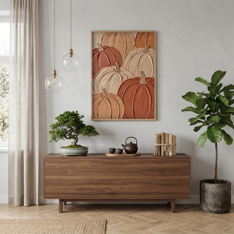 May include: A rectangular framed wall art piece featuring a textured, impasto-style painting of multiple pumpkins in shades of orange, terracotta, and cream. The artwork is displayed above a long, dark wood sideboard with a bonsai tree and tea set.