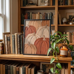 May include: A framed wall art piece featuring a textured impasto painting of multiple pumpkins in shades of cream, beige, tan, and burnt orange. The artwork is displayed in a thin black frame, showcasing thick, raised paint strokes throughout.