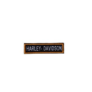 May include: A rectangular patch with the words "HARLEY-DAVIDSON" embroidered in white on a black background. The patch has a gold border and is set against a white background.
