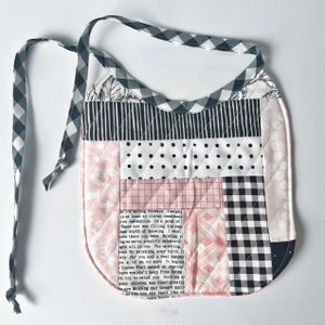 May include: A pink and black patchwork baby bib with a black and white checkered trim. The bib has a tie closure and features a printed text that reads: "ke I'm moving forward Tonight is at home my clever sweetheart ion redemption In a pond of There now was filling the enp then depth of knowing I want Grow there you were Holding y ing we serve simplify celebrate gth all in one The catching, rish My sunshine, your birth it uty for you and a real compar ou a of me, no more It begint listen What seemed so improbe here wouldn't keep fron being re, try to catch you Nothing si good shining sun Discriminatio ho are Holding our breath and so you are now feels like"