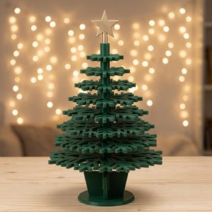 Pode incluir: Um enfeite de árvore de Natal verde-escuro de vários níveis, construído com camadas empilhadas em forma de floco de neve. A árvore apresenta um poste central vertical e é rematada com uma única estrela dourada de cinco pontas na base.