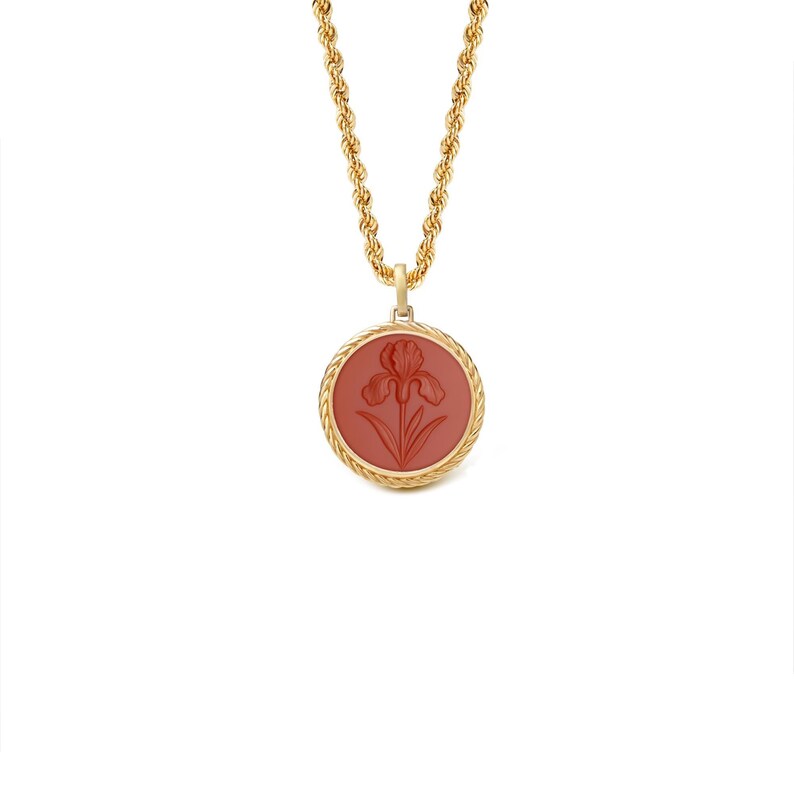 May include: A gold-toned necklace with a rope chain and a round pendant. The pendant features a red-orange iris flower design within a gold border. The necklace is displayed against a white background.