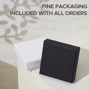 May include: Two square gift boxes, one white and one black, are displayed on a white surface. The black box is open, revealing its interior. The text "FINE PACKAGING INCLUDED WITH ALL ORDERS" is visible above the boxes.