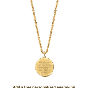 May include: Gold-colored necklace with a round pendant. The pendant has the engraved text: "The harder you work for something, the greater you'll feel when you achieve it." The necklace chain is a rope style.