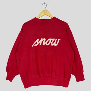 Può includere: Felpa rossa con una grafica bianca "SNOW" sul davanti.