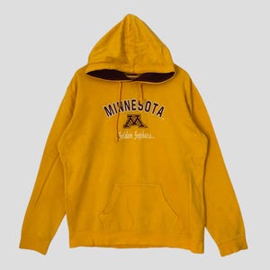 May include: Mustard yellow hooded sweatshirt with the word "MINNESOTA" arched across the chest in brown lettering. Below the word "MINNESOTA" is a brown "M" logo and the words "Golden Gophers". The sweatshirt has a kangaroo pocket.