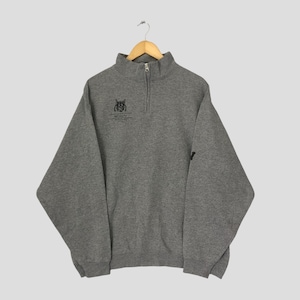 Puede incluir: Una sudadera gris con cremallera de cuarto de cierre, con un pequeño logotipo negro en el pecho y un pequeño logotipo negro en la manga. El logotipo del pecho presenta un búho estilizado y la palabra "Wizards". La sudadera está colgada de una percha de madera.