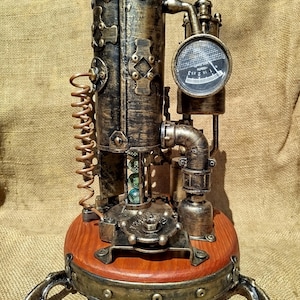 Może przedstawiać: Rzeźba w stylu steampunk z cylindrycznym korpusem, stożkowym wierzchołkiem i okrągłym wskaźnikiem. Rzeźba wykonana jest z metalu z brązowym i miedzianym wykończeniem i stoi na drewnianej podstawie z metalowymi nogami. Rzeźba ma styl vintage i industrialny.