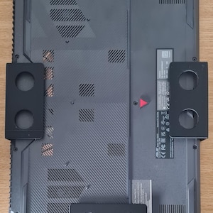 May include: Black laptop stand with two sets of holes on each side. The stand is holding a black laptop with a silver sticker on the back. The sticker has text that reads "ASUS, FCC ID: 2A3L-X571, IC: 6638A-X571".