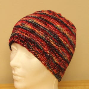 Pode incluir: Um chapéu de malha listrado em tons de vermelho, laranja, amarelo, azul e preto. O chapéu está em uma cabeça de manequim branca.