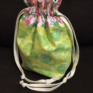 May include: A white drawstring bag with a lime green and yellow print of lime slices. The bag has white drawstrings with knots at the ends.