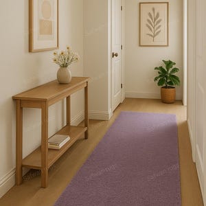 May include: A hallway with a light purple rectangular rug, a wooden console table, and framed artwork. The walls are painted a neutral color, and the floor is hardwood. A vase of flowers sits on the table, and a potted plant is visible.