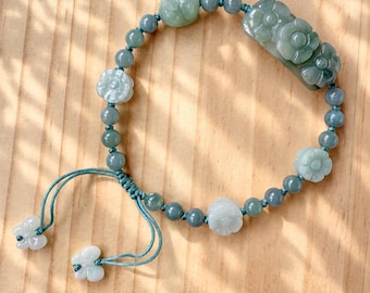 May include: A bracelet featuring light green jade beads, carved flower-shaped jade accents, and a larger rectangular jade piece with floral carvings. The beads are strung on a teal cord with an adjustable sliding knot and two small butterfly-shaped jade charms at the ends.