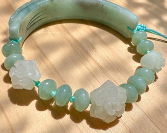 May include: A bracelet featuring a curved, light green jade segment with carved lines, connected by a light blue cord to a series of round, pale green jade beads and two carved, off-white floral jade beads arranged in a circular pattern.