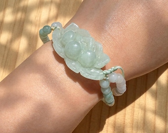 May include: A light green jade bracelet featuring a central carved floral motif with rounded petals and smooth, polished surfaces. The bracelet is constructed from small, round, translucent beads strung on a thin, adjustable cord.