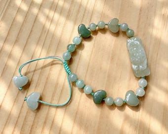 May include: A bracelet featuring light green jade beads, heart-shaped jade accents, and a central carved jade charm. The piece is strung on a light green cord with an adjustable sliding knot closure, finished with two small heart-shaped jade beads.