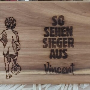 Könnte beinhalten: Ein Holzbrett mit einem Design eines Jungen, der Fußball spielt, und dem Text "So sehen Sieger aus Vincent".