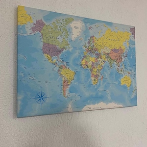 May include: A blue and yellow world map with country borders and names printed on a canvas. The map includes a compass and the words "Pacific Ocean", "North Atlantic Ocean", "South Atlantic Ocean", "Antarctica", "Russia", "Canada", "United States", and "Brazil".