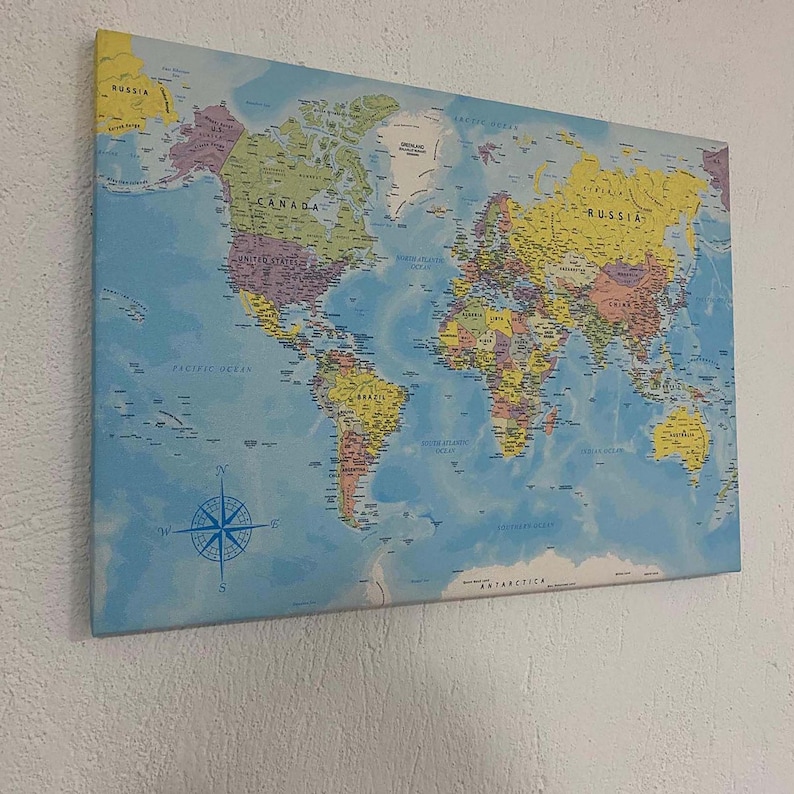 May include: A blue and yellow world map with country borders and names printed on a canvas. The map includes a compass and the words "Pacific Ocean", "North Atlantic Ocean", "South Atlantic Ocean", "Antarctica", "Russia", "Canada", "United States", and "Brazil".