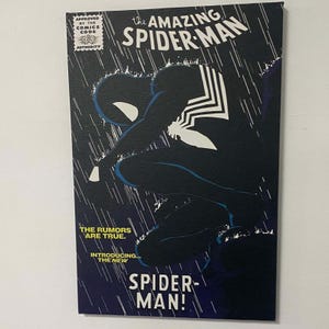 Puede incluir: Impresión en lienzo de una portada de cómic con el Amazing Spider-Man. La obra de arte representa a Spider-Man con un traje negro, agachado bajo la lluvia. El texto incluye "The Amazing Spider-Man" y "Introducing... The New Spider-Man!"