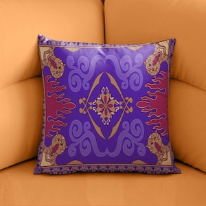 May include: Purple and gold throw pillow with a design of a magic carpet from the movie Aladdin. The carpet has a repeating pattern of flames and swirls.