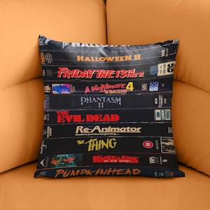 May include: A decorative pillow featuring a stack of vintage VHS tapes. Titles include "Halloween II", "Friday the 13th", "A Nightmare 4", "Phantasm II", "The Evil Dead", "Re-Animator", "The Thing", "Nightmare on Elm Street", and "Pumpkinhead".