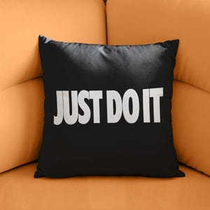 May include: Black square pillow with the white text "JUST DO IT". The pillow is on an orange couch. The pillow is a decorative item.
