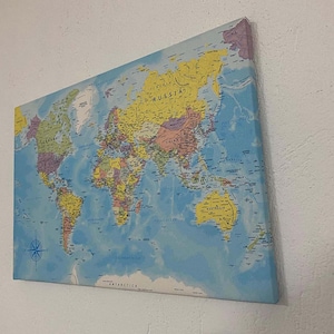 May include: A blue and yellow world map printed on canvas. The map shows the continents and oceans of the world. The map is framed and ready to hang on a wall.