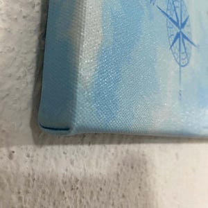 May include: Close-up of the edge of a blue canvas painting with a white border. The canvas has a textured surface.