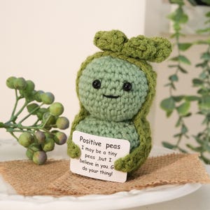 Peut inclure: Un jouet en peluche de pois vert crocheté tenant une pancarte qui dit "Positive peas I may be a tiny peas, but I believe in you. Go do your thing!"