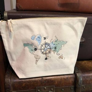 Peut inclure: Une pochette zippée en toile blanche avec un motif de carte du monde et de boussole brodé en couleur.