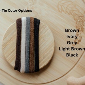Pode incluir: Um close-up de seis el&aacute;sticos de cabelo em diferentes cores: marrom, marfim, cinza, marrom claro e preto. Os el&aacute;sticos de cabelo est&atilde;o dispostos em c&iacute;rculo sobre uma superf&iacute;cie de madeira.