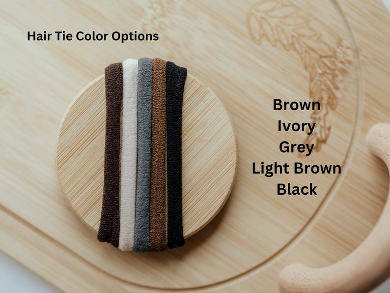 Pode incluir: Um close-up de seis el&aacute;sticos de cabelo em diferentes cores: marrom, marfim, cinza, marrom claro e preto. Os el&aacute;sticos de cabelo est&atilde;o dispostos em c&iacute;rculo sobre uma superf&iacute;cie de madeira.