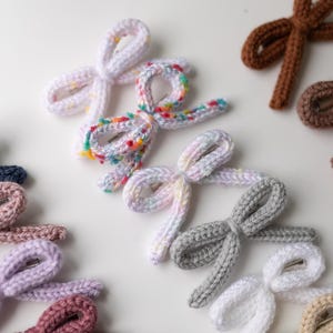 Pode incluir: Conjunto de la&ccedil;os de cabelo de malha feitos &agrave; m&atilde;o em v&aacute;rias cores, incluindo rosa, roxo, azul, marrom e branco. Os la&ccedil;os s&atilde;o amarrados com um n&oacute; simples e t&ecirc;m um pequeno clipe de metal preso na parte de tr&aacute;s.