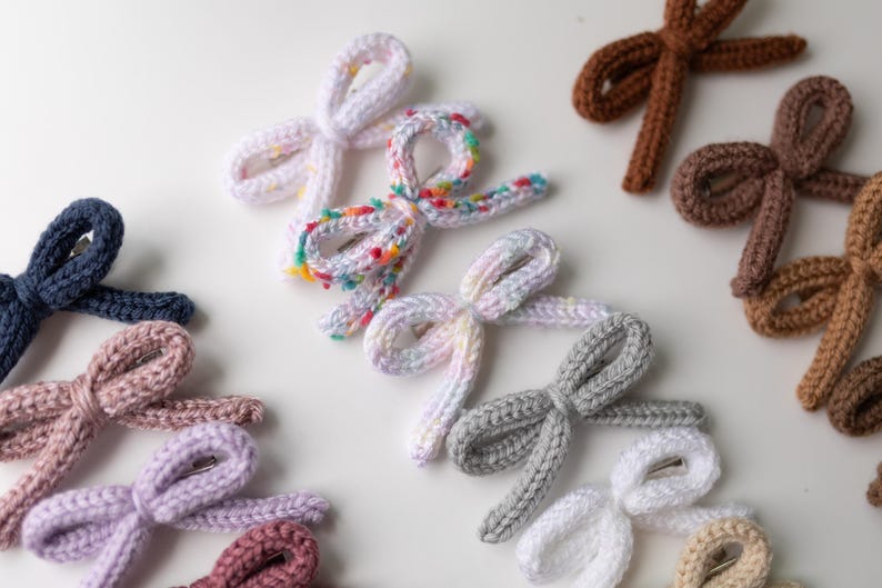 Pode incluir: Conjunto de la&ccedil;os de cabelo de malha feitos &agrave; m&atilde;o em v&aacute;rias cores, incluindo rosa, roxo, azul, marrom e branco. Os la&ccedil;os s&atilde;o amarrados com um n&oacute; simples e t&ecirc;m um pequeno clipe de metal preso na parte de tr&aacute;s.