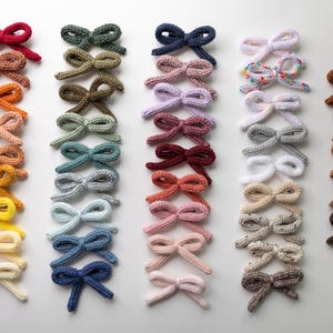 Pode incluir: Uma cole&ccedil;&atilde;o de 30 la&ccedil;os de tric&ocirc; feitos &agrave; m&atilde;o em v&aacute;rias cores, incluindo vermelho, verde, azul, rosa, amarelo, marrom e branco. Os la&ccedil;os est&atilde;o dispostos em filas sobre uma superf&iacute;cie branca.