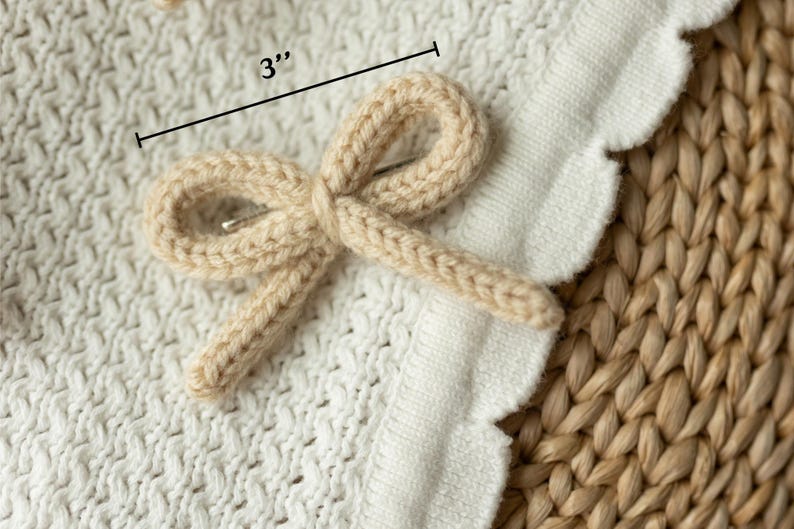 Pode incluir: Um prendedor de cabelo de la&ccedil;o de malha bege, medindo 7,6 cm de comprimento, &eacute; exibido em uma superf&iacute;cie de malha branca.