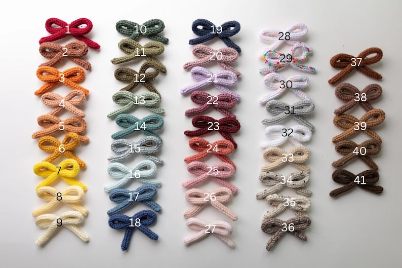 Pode incluir: Quarenta e um la&ccedil;os de malha feitos &agrave; m&atilde;o em v&aacute;rias cores, incluindo vermelho, verde, azul, rosa, marrom e branco. Os la&ccedil;os est&atilde;o dispostos em filas, numeradas de 1 a 41.