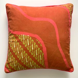 May include: A red and pink pillow with a green and white patterned design. The pillow has a pink border.