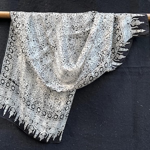 May include: A white and black patterned fabric with a floral design. The fabric is draped over a wooden rod.