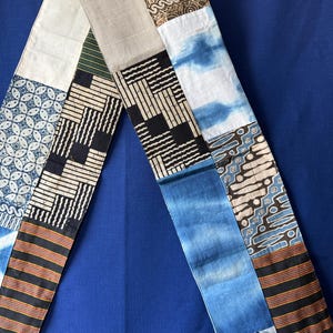 Peut inclure: Un long chemin de table rectangulaire composé d'un assemblage de tissus variés. Les motifs incluent du batik bleu et blanc, des rayures géométriques noires et blanches, du beige uni, du tie-dye indigo et des rayures horizontales multicolores.