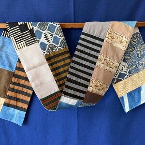 Peut inclure: Un long chemin de table rectangulaire composé d'un assemblage de divers motifs textiles. La pièce présente des sections aux imprimés géométriques noirs et blancs, des rayures bleues et brunes, des motifs floraux et des panneaux unis dans des tons bleus et beiges.