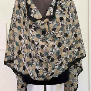 Peut inclure: Un châle à motifs noir et blanc avec un design de cercles superposés de turquoise, marron et or. Le châle est drapé sur un mannequin noir.